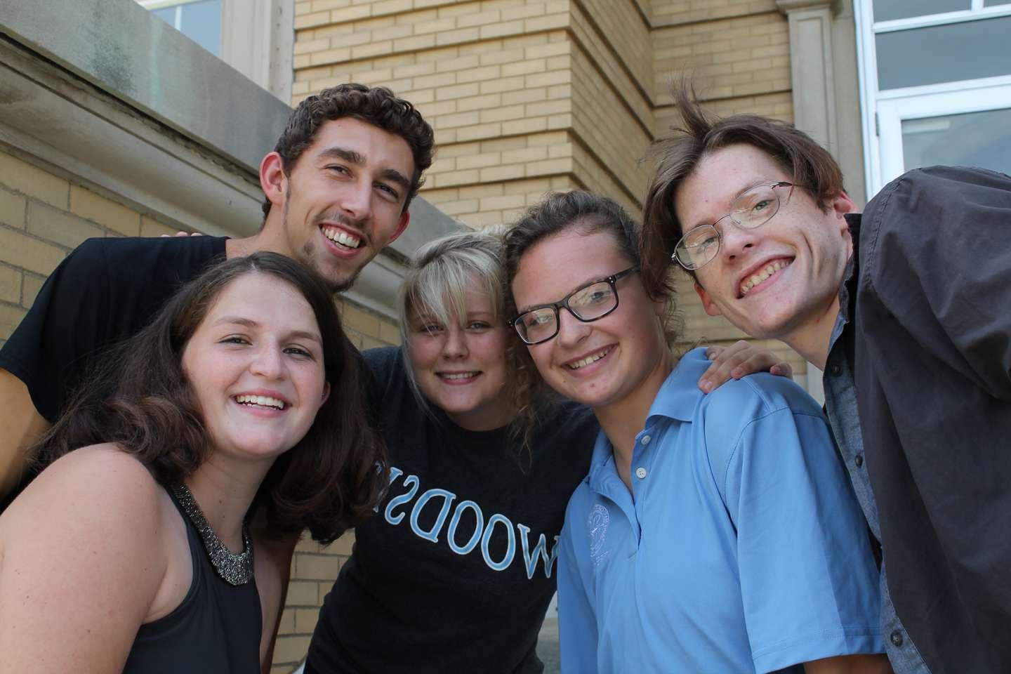 Two males and three females with their heads together smiling.